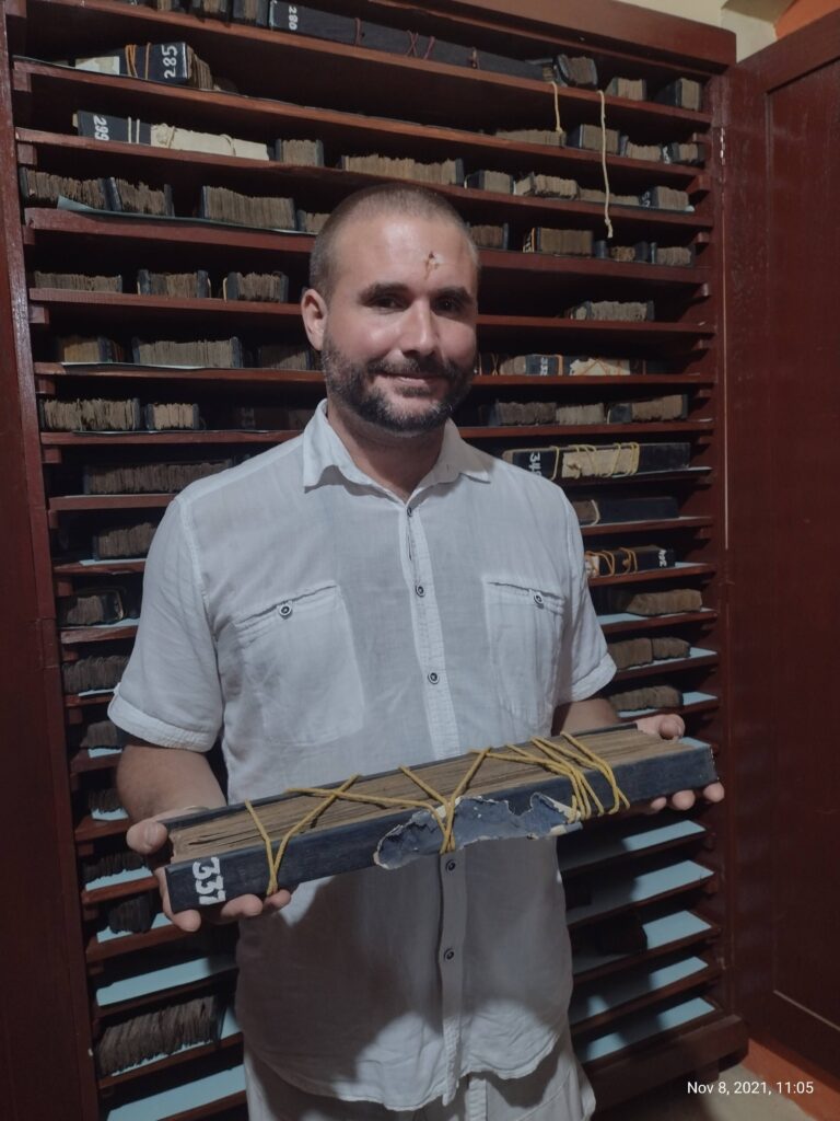 Stephan holding a bundle of palm leaves in a palm leaf library in India